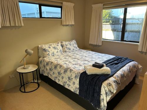 a bedroom with a bed and a lamp and windows at Mount Maunganui House -Walk to Beach, Shops, Cafés in Mount Maunganui