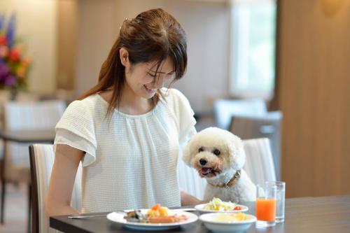 a woman sitting at a table with a white dog at Izumigo Toba Dog Paradise Hotel in Toba