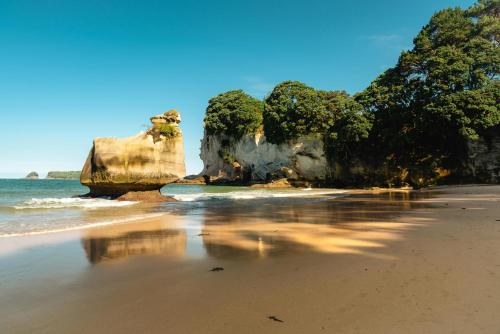 a beach with a large rock in the water at Whitianga Coastal Stay, Cosy Studio at Oceans Resort in Whitianga