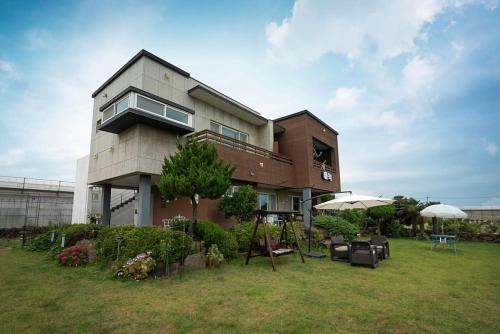 a large house with chairs and tables in a yard at Jeju Aneuk Stay in Murŭng-ni