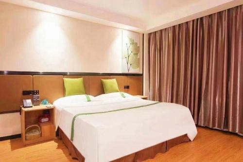a bedroom with a large white bed with green pillows at GreenTree Inn Puyang Pushang Huanghe Road in Puyang