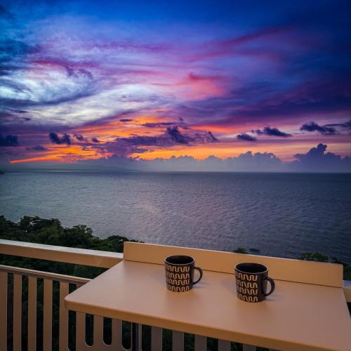 two coffee mugs sitting on a table with a sunset at Aqua Horizon Beachside Condo I Signature Art Suites in Dauis