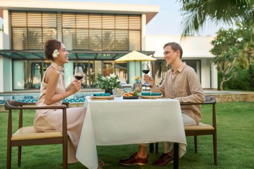 a man and woman sitting at a table with wine glasses at Wyndham Grand Phu Quoc in Phu Quoc