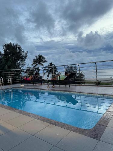 a swimming pool with people sitting on benches next to it at The Sea by Club Travalet in Alleppey