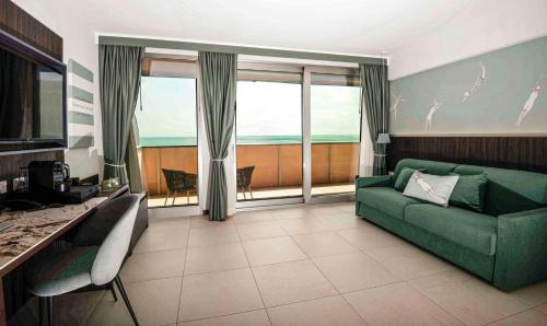 a living room with a green couch and large windows at Hotel Europa Lignano in Lignano Sabbiadoro