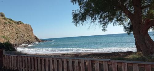 a beach with a fence and a tree and the ocean at Aggeliki's Beach Escape Above the Sea - Northern Chios in Límnos