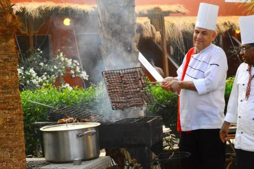 a man standing next to a grill with a pot of food at Sun Beach Hotel ABO SOMA in Hurghada