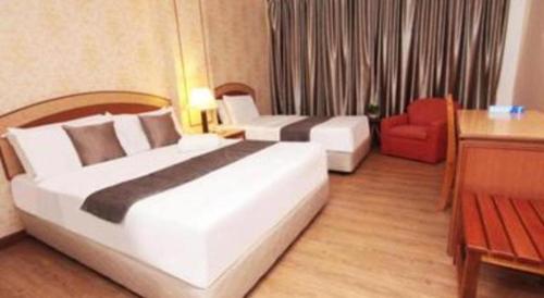 a hotel room with two beds and a red chair at Pelican Hotel in Batu Pahat