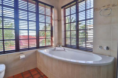 a bathroom with a tub and a toilet and windows at North Hill Guesthouse in Bloemfontein