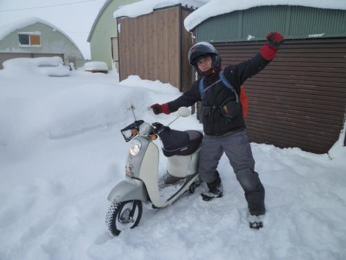 a man standing next to a scooter in the snow at Akane-yado in Nakafurano