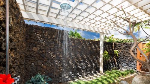 a white pergola over a stone wall with a waterfall at ❤PiH❤ Hale Kanani Hilton Resort PassesFully Detached HomeBeach Gear Bikes in Waikoloa