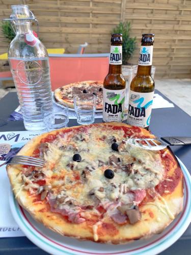 deux pizzas sur une table avec deux bouteilles de bière dans l'établissement Emplacement tente, caravane 120 m2, à Chauzon