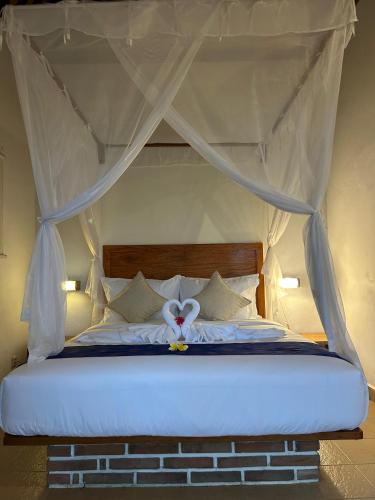 a bedroom with a canopy bed with white sheets and pillows at Rumah Tenun in Karangasem