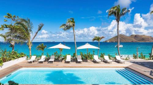 a pool at the beach with chairs and umbrellas at Luxurious Beachfront Villa in Flamands in Anse des Flamands