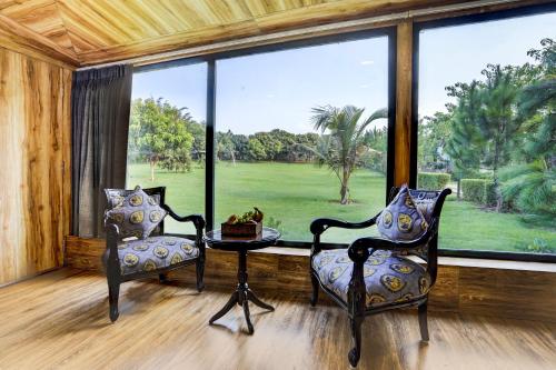 a room with two chairs and a table and a large window at Alaya Stays Fortezza Pet-friendly 6-BHK Farmhouse With Private Pool, Gazebo & Lush Garden in Bhundsi