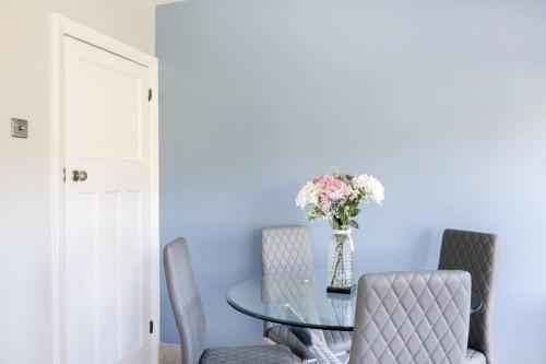 a dining room with a glass table with chairs and a vase of flowers at Ladybird House in Loughborough