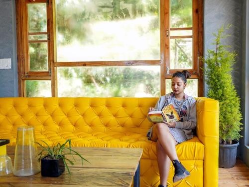 a woman sitting on a yellow couch reading a book at The Hosteller Mcleodganj, Upper Bhagsu in McLeod Ganj