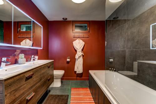 La salle de bains est pourvue de murs rouges, d'une baignoire et d'un lavabo. dans l'établissement Chalet Hibou, à Chamonix-Mont-Blanc