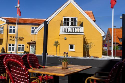 a table and chairs on a balcony with a yellow house at Plesners Badehotel in Skagen