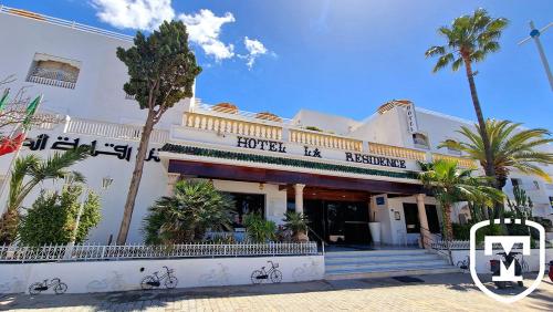 a white building with palm trees in front of it at Hotel La Residence Hammamet in Hammamet