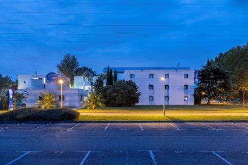 a parking lot in front of a building at night at The Originals Access, Hôtel Innostar in Labège
