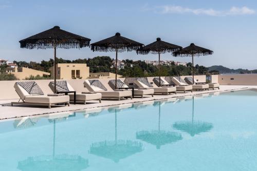 a row of chairs and umbrellas next to a swimming pool at Physis Oikos Beachfront Apartments in Skiathos