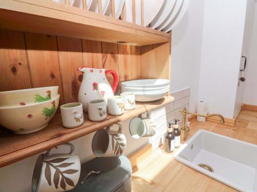 a kitchen with a shelf with cups and a sink at Lavender Cottage in Helston