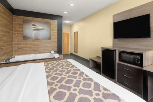 a hotel room with a bed and a tv and a tub at Baymont by Wyndham Paw Paw in Paw Paw