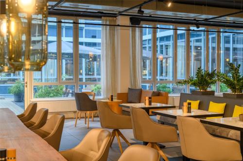 a restaurant with tables and chairs and windows at Flightgate Munich Airport Hotel, a member of Radisson Individuals in Hallbergmoos