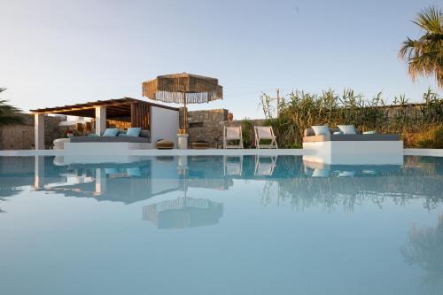 a swimming pool with chairs and an umbrella in front of a house at Myconian Theros Luxury Suites in Ano Mera