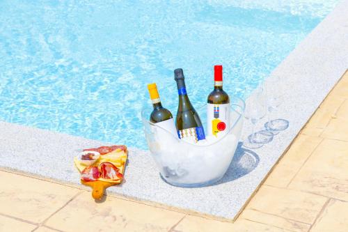 a basket of wine bottles and a pizza next to a swimming pool at Dimora PietrAnna - Paradiso in Sardegna in Li Valcaggi