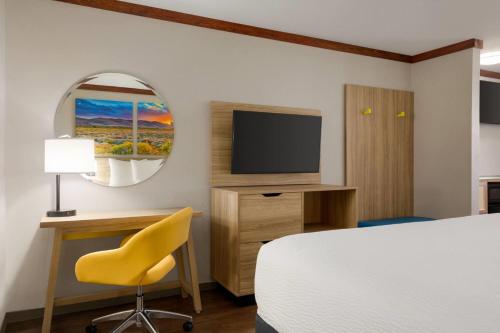 a hotel room with a bed and a desk and a television at Days Inn by Wyndham Suites Fredericksburg in Fredericksburg
