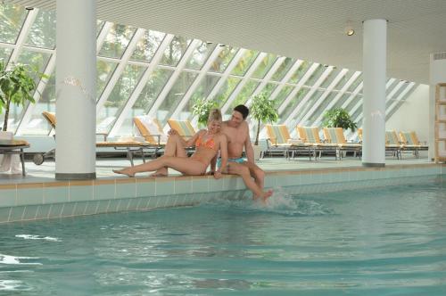 a man and a woman sitting next to a swimming pool at Best Western Premier Parkhotel Bad Mergentheim in Bad Mergentheim