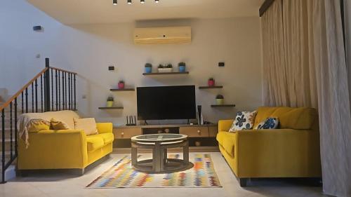sala de estar con 2 sofás amarillos y TV en Marassi Villa Twinhouse, en El Alamein