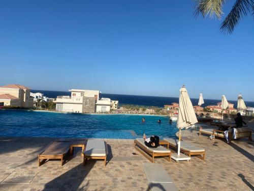 a pool with chairs and an umbrella and people in the water at Cozy studio in Azzurra Resort Sahl Hasheesh 65 Sq M in Hurghada