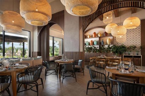 a restaurant with wooden tables and chairs and chandeliers at Zemi Miches Punta Cana All-Inclusive Resort, Curio by Hilton in Miches