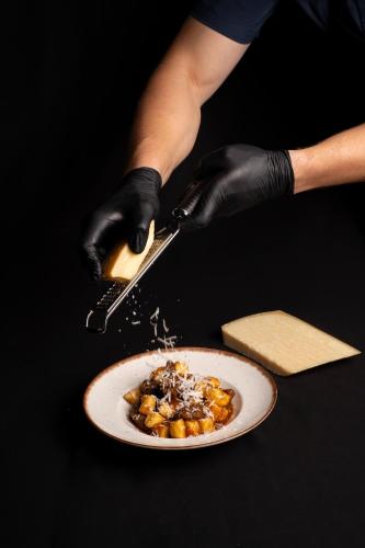 a person in black gloves holding a knife and a plate of food at Hotel Marina in Fažana