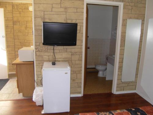 a bathroom with a toilet and a tv on a wall at Virden Motel in Virden