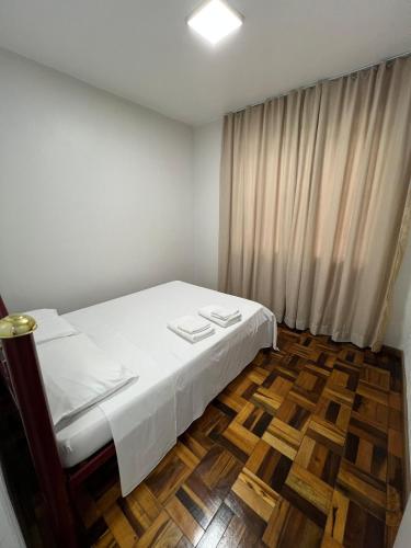 a bedroom with a white bed and a wooden floor at Aconchegante apto no Centro! in Concordia