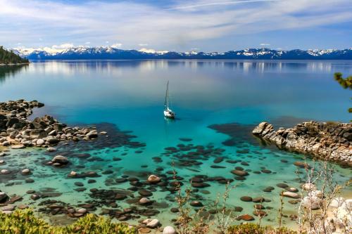 a boat in a lake with mountains in the background at VIP Lakefront Condo Amazing Views Pool Pickleball Excellent Location Balcony BBQ in Kings Beach