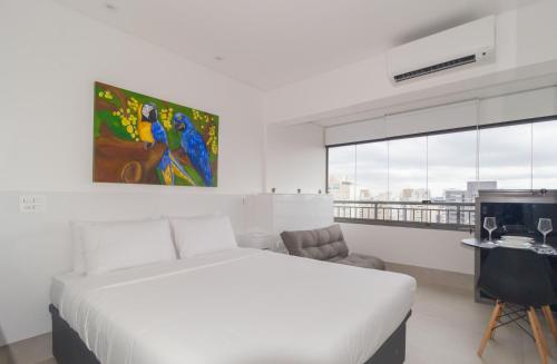 a white bedroom with a bed and a desk and window at Prime Grand Vitrali Moema in Sao Paulo