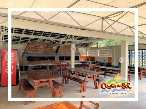 Una cafetería con mesas y sillas de madera y una máquina de Coca-Cola. en Hospedagem em Canasvieiras - Pé na Areia com Vista para o Mar, en Florianópolis