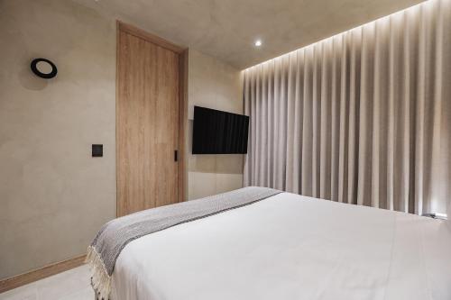 a bedroom with a white bed and a flat screen tv at Kuuna Luxury Stays by Wynwood House in Medellín