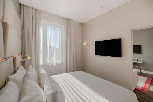 a bedroom with a bed with white pillows and a television at NH Collection Palazzo Cinquecento in Rome