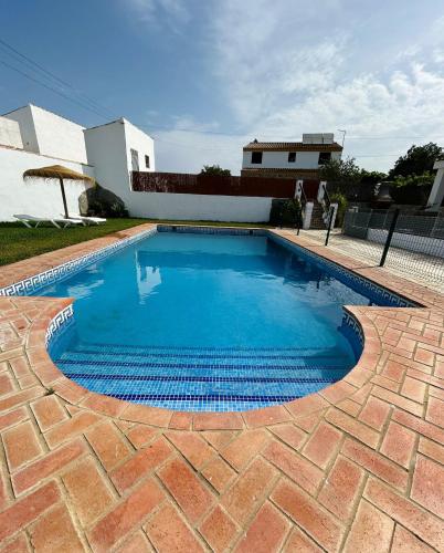 a swimming pool with a brick floor and a house at Chalet con piscina privada grupos in Conil de la Frontera