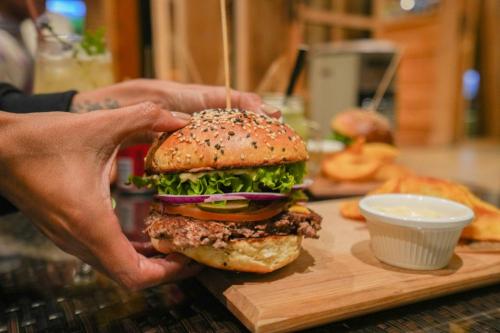 a person holding a hamburger on a cutting board at Alto Melimoyu Hotel & Patagonia in La Junta