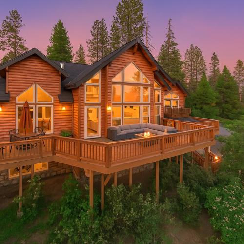 a log cabin with a large deck at dusk at Sunset Mountain Hot Tub, Fire Table, Epic Views in Shaver Lake