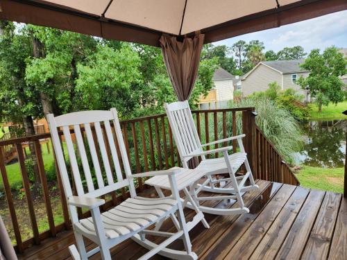 two rocking chairs on a deck with an umbrella at Savannah Lakefront Retreat near Tybee Beach with King Bed and Free Parking in Savannah