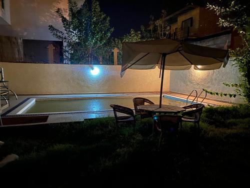 una sombrilla y sillas junto a una piscina por la noche en Villa à louer Nouaceur 3 chambre avec piscine privée, en Nouaseur