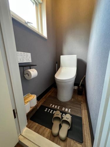 a bathroom with a toilet and two shoes on a rug at ヴィラYukara緑屋 in Nanae